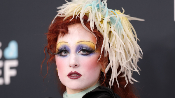 Chappell Roan appears at the Grammys in purple and yellow eye makeup skinny brows and a feathered headpiece.